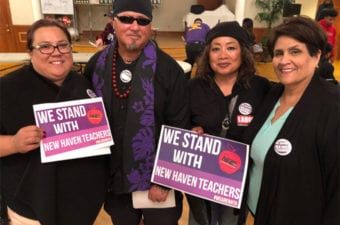 People standing inside room holding signs in support of New Haven Teachers