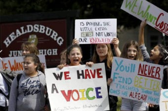 People and kids standing outside holding up colorful protest signs in front of Junior High School