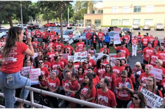 People standing in a parking lot all wearing red shirts a person sitting on a bar talking in mic