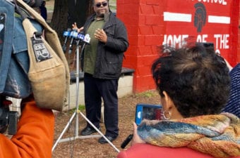 Man standing outside at a new conference with other people looking on