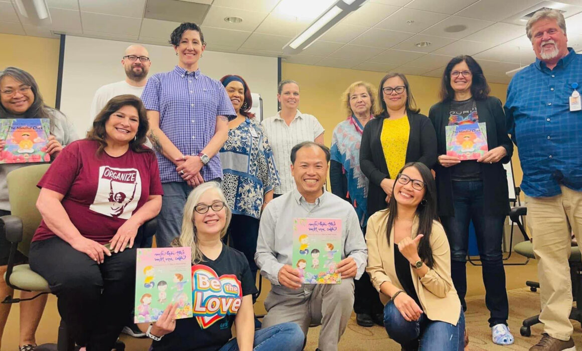 Thirteen people pose for a photograph while holding up books,