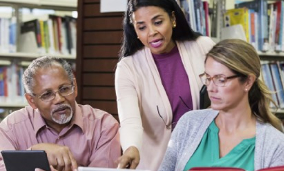 Photo of three professional adults talking at a desk