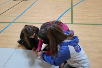An image of three young students looking down at a table while working on a project.