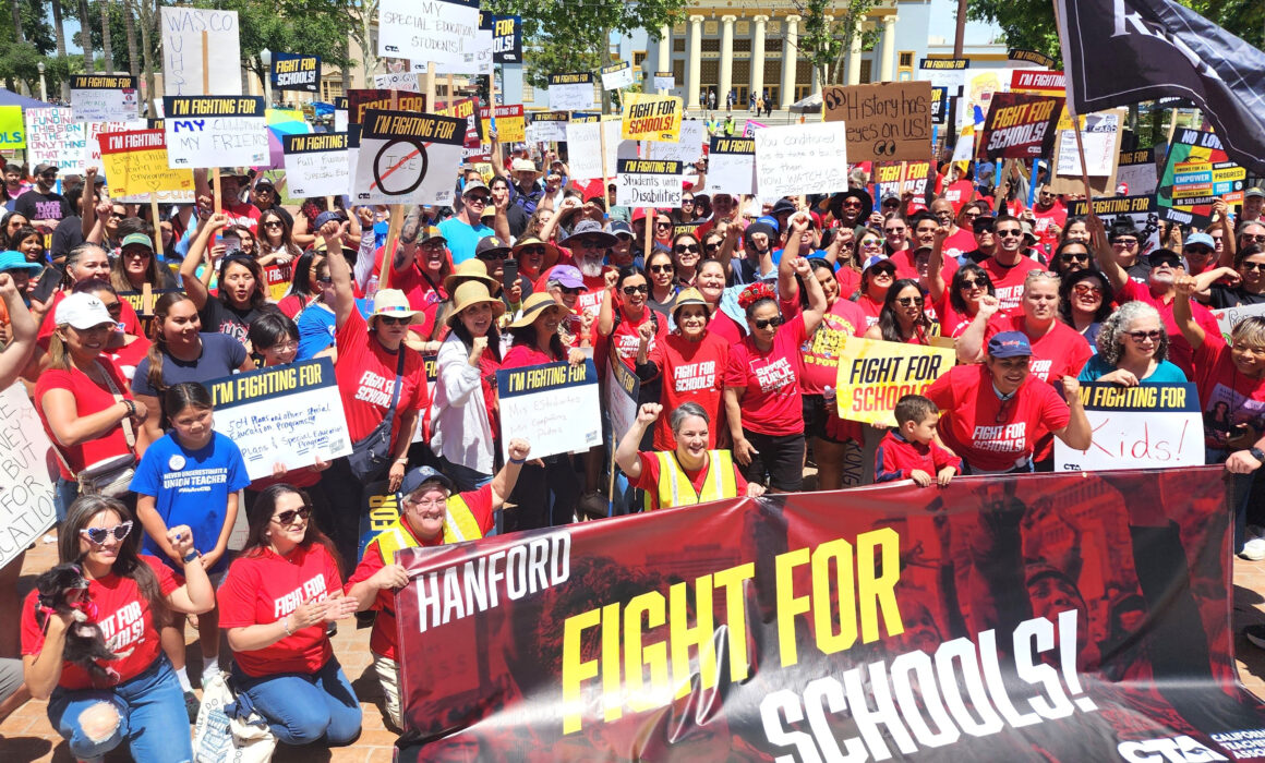 Photo of a large crowd of people holding protest signs in front of a large banner that says "Fight For Schools".